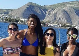 Durante il tour privato in barca "Scegli l'itinerario" da Agios Georgios organizzato da Crazy Sports, un gruppo di amici posa per una foto con gli spettacolari paesaggi vulcanici dell'isola sullo sfondo.