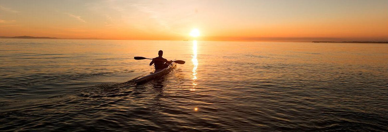 Un chico haciendo kayak durante la puesta de sol con nuestro alquiler de kayaks en Ibiza.