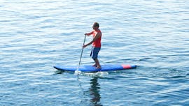Durante el curso privado de Paddle Surf, um hombre rema en las aguas tranquilas bajo la supervisión de un instructor certificado de Surfaventura.