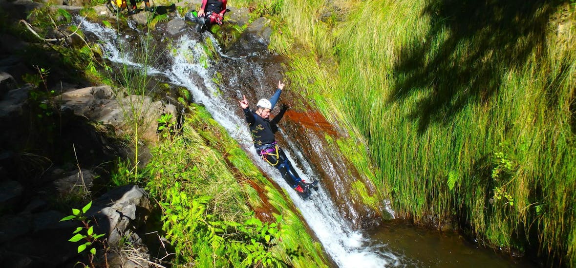 Een deelnemer aan de Canyoning voor Beginners op Madeira met Epic Madeira heeft plezier terwijl hij van een natuurlijke waterglijbaan afglijdt.