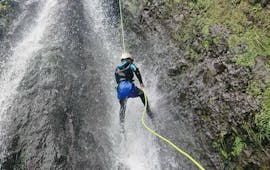 Pendant le canyoning de niveau Intermédiaire à Madère avec Epic Madeira, un participant descend courageusement en rappel au-dessus d'une chute d'eau orageuse.