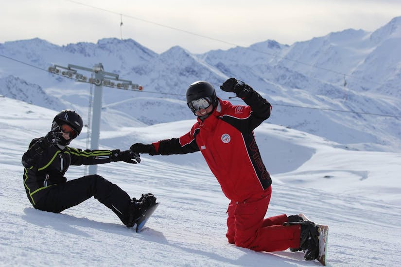 An instructor is helping his student and waving during their kids and adult snowboaring lessons for beginners at skischule Obergurgl.