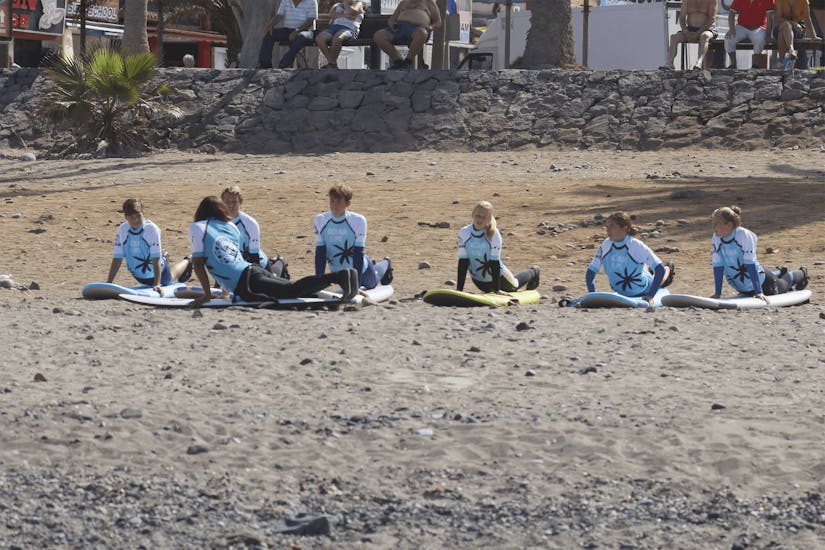 Die Teilnehmer des Surfkurses in Playa de las Américas für Fortgeschrittene mit Ocean Life Surf School wärmen sich am Strand für den Unterricht auf.