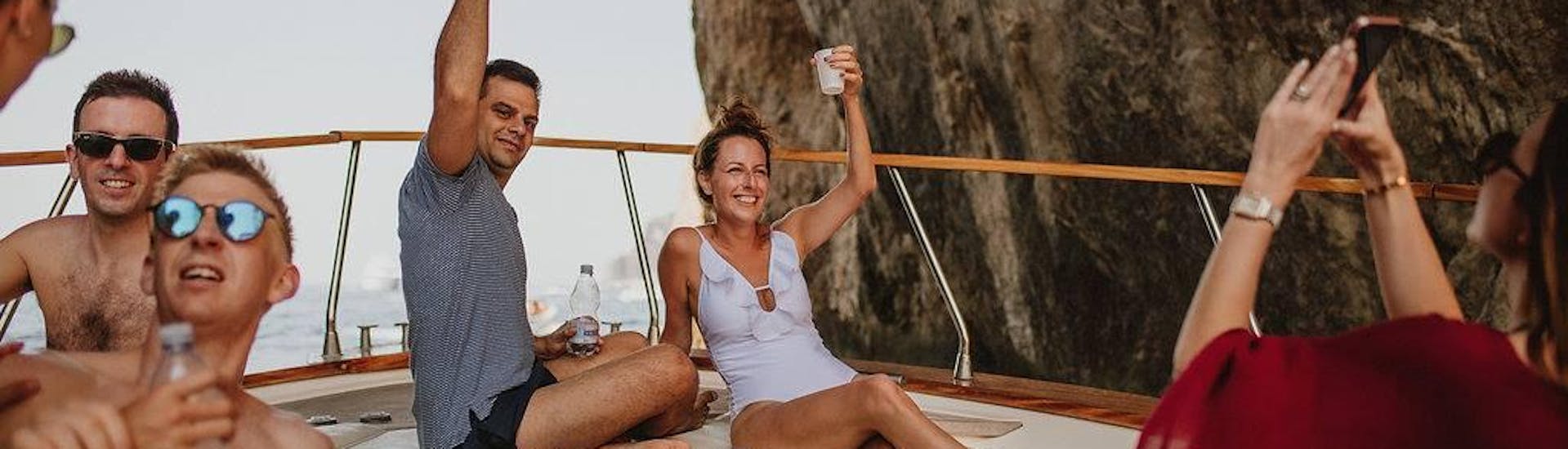 Menschen, die jubelnd auf einem Boot liegen und mit Getränken in der Hand, während einer privaten Bootsfahrt um die Insel Capri mit dem Capitano Ago Costiera Amalfitana.