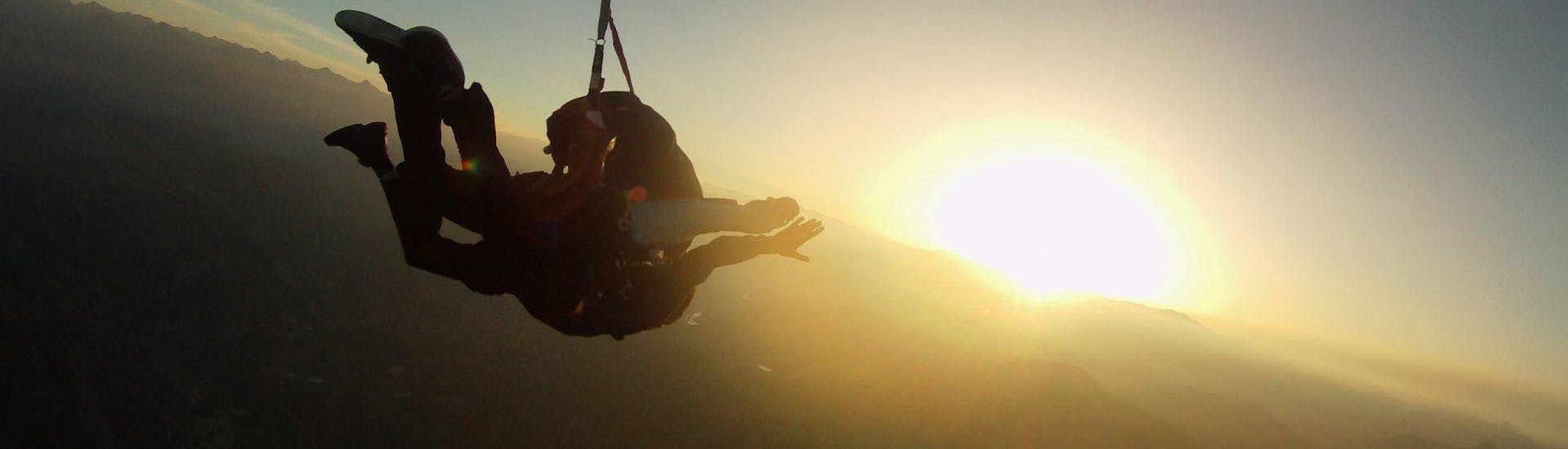 Un pilote de tandem de Skydive Center saute en parachute avec un passager à une altitude de 4 000 m à Gap-Tallard sous le coucher du soleil.