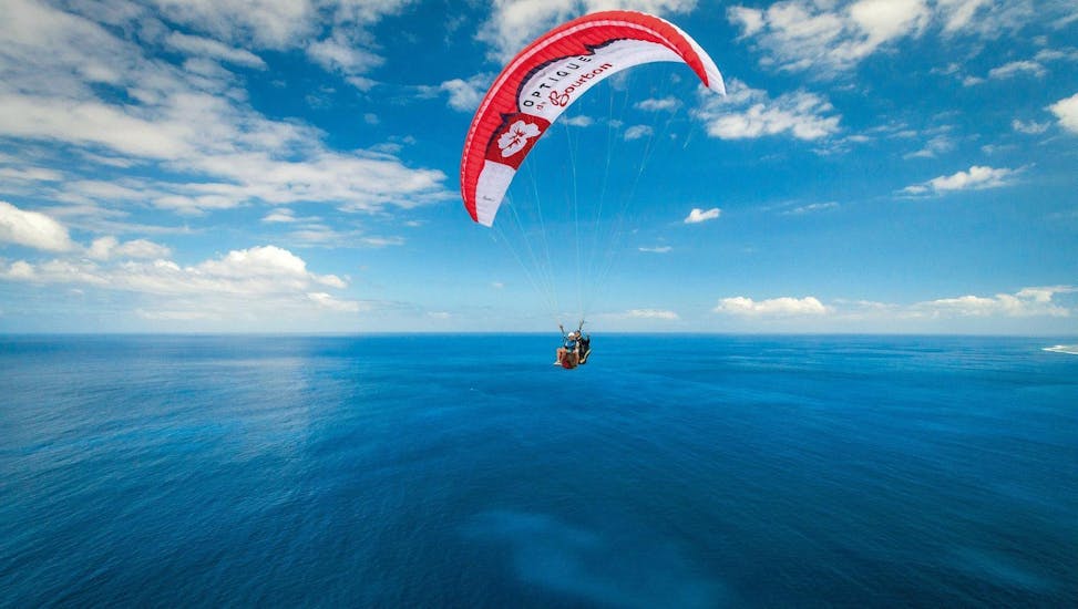 A paraglider pilot from Addict Parapente is flying over the Bay of St Leu during a Tandem Paragliding Flight "You Steer".