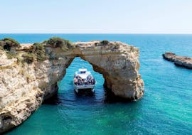 During the catamaran tour from Vilamoura to Caves of Benagil, tourist are passing under a rock formation aboard a modern catamaran from Ocean Quest.