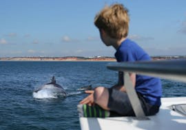 During a catamaran tour from Vilamoura, a small boy is watching jumping dolphins whilst relaxing abord a modern catamaran from Ocean Quest.