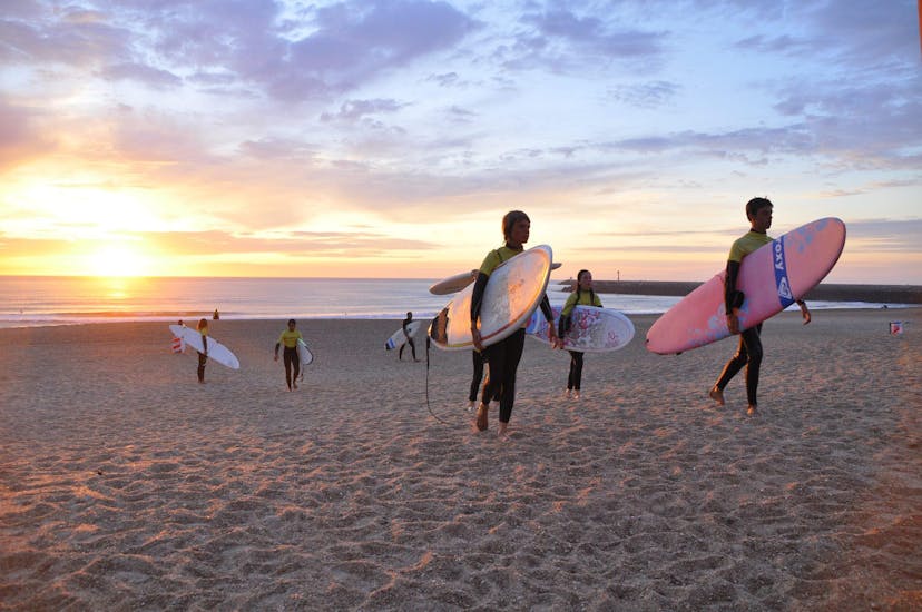 Un grupo de jóvenes surfistas en la playa al atardecer.