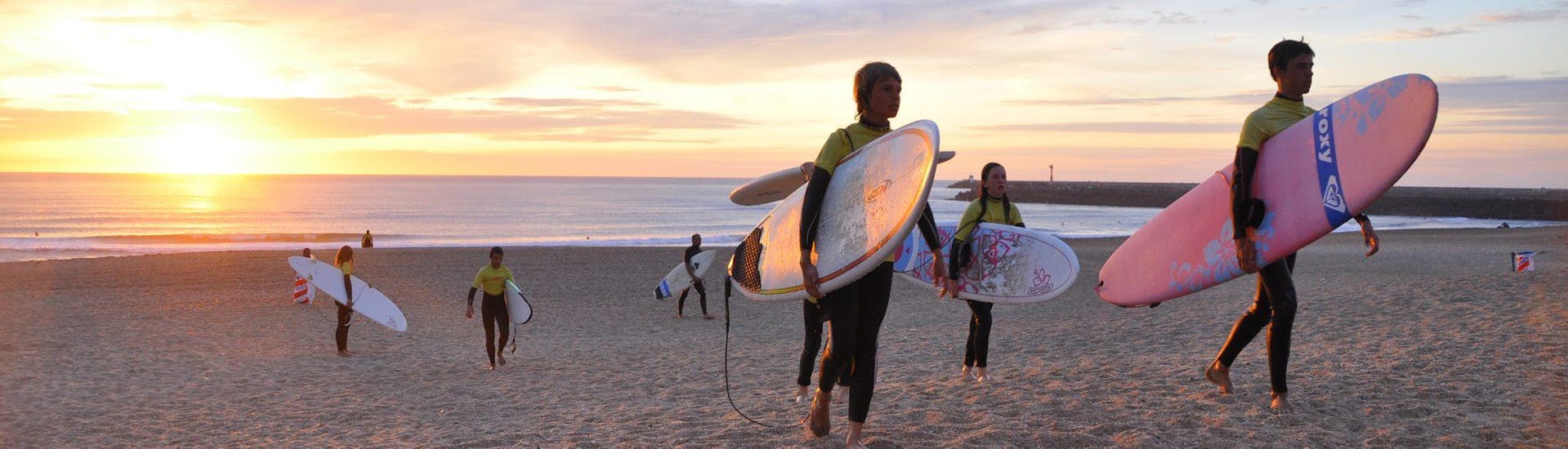 Een groep jonge surfers op het strand bij zonsondergang.