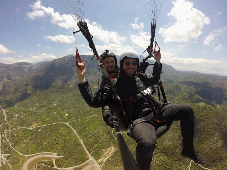 During the tandem paragliding above Chania, a man is having a great time flying safely with a certified tandem pilot from Cretan Paragliding.