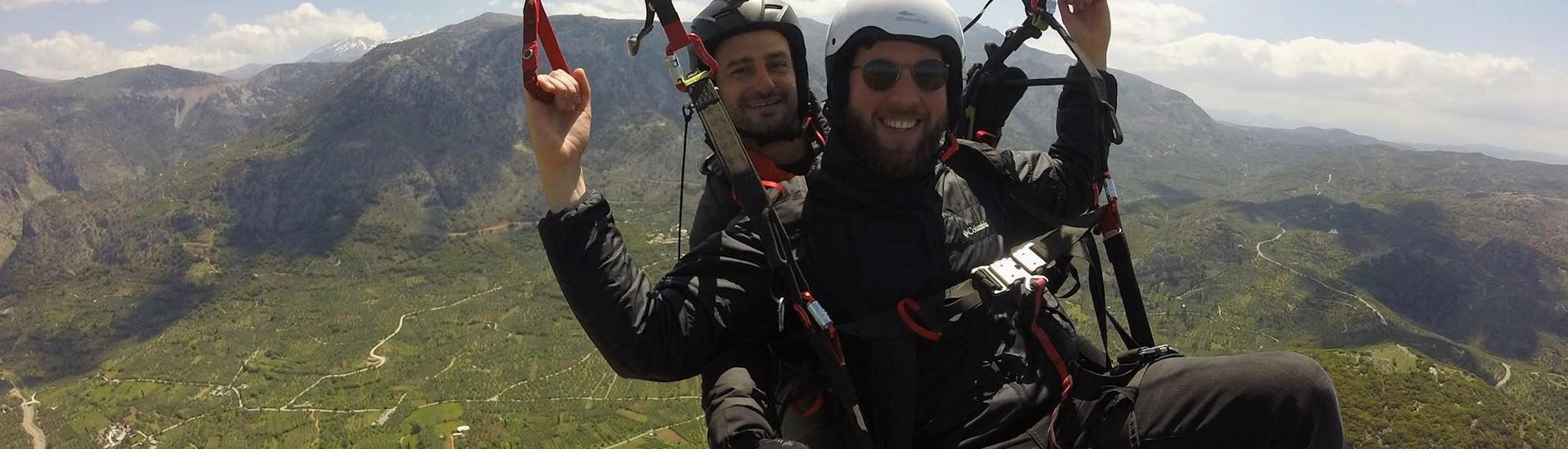 During the tandem paragliding above Chania, a man is having a great time flying safely with a certified tandem pilot from Cretan Paragliding.