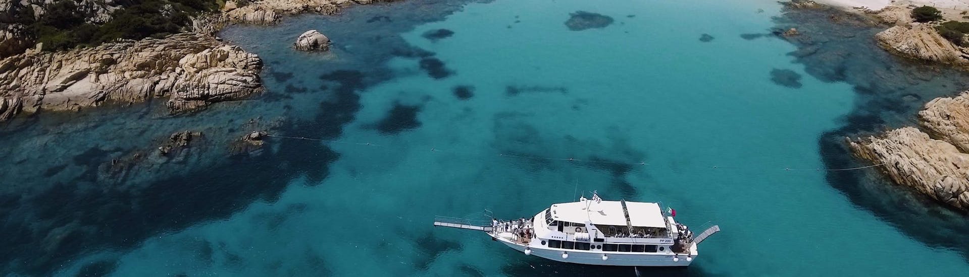 Una bella e spaziosa barca naviga attraverso la baia durante la gita in barca delle 4 isole all'arcipelago di La Maddalena da Palau.