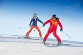 Eine Frau fährt während eines privaten Skikurs für alle Alters- und Leistungsstufen bei der Skischule Tritscher mit ihrem Skilehrer einen Hang im Pflug hinunter.