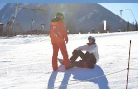 Een skileraar van skischool Tritscher geeft een zittende snowboarder instructies tijdens zijn privé snowboardlessen voor alle leeftijden en niveaus.