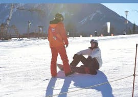 An instructor from skischule Tritscher is instructing a snowboarding sitting on the ground during his Private Snowboarding Lessons for All Levels & Ages.