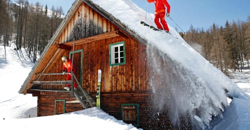 Privater Freeride Kurs für Erwachsene aller Levels mit Skischule Tritscher Schladming Zwei Skifahrer fahren über das Dach einer Hütte während ihres privaten Skikurses abseits der Piste für Erwachsene aller Stufen mit der Skischule Tritscher.