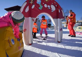 Three children are playing together with an instructor during their kids ski lessons "miniclub" at Skischule Tritscher in Planai.