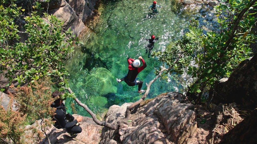 Un participant à la sortie Canyoning "Découverte" - Canyon de Pulischellu saute dans une piscine naturelle vert émeraude sous la supervision d'un guide de canyoning qualifié d'Acqua et Natura.