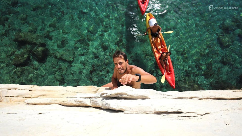 Voordat de zon begint te verdwijnen, beklimt een man een rots tijdens een zeekajaktocht bij zonsondergang met snorkelen georganiseerd door Adventure Dalmatia Dubrovnik.
