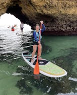 Eine junge Frau steht auf ihrem Brett während der geführten Stand Up Paddle Tour entlang der Küste von Albufeira mit SUPA Sea Adventures Algarve.