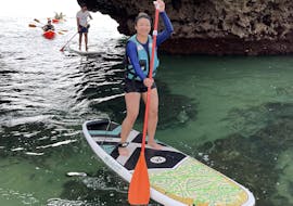 Una giovane donna in piedi sulla sua tavola durante il Tour guidato in Stand Up Paddle lungo la costa di Albufeira con SUPA Sea Adventures Algarve.