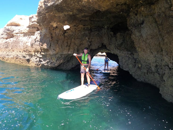 A young man is doing stand up paddle during a Guided Stand Up Paddle Tour along the Albufeira Coast with with SUPA Sea Adventures Algarve.