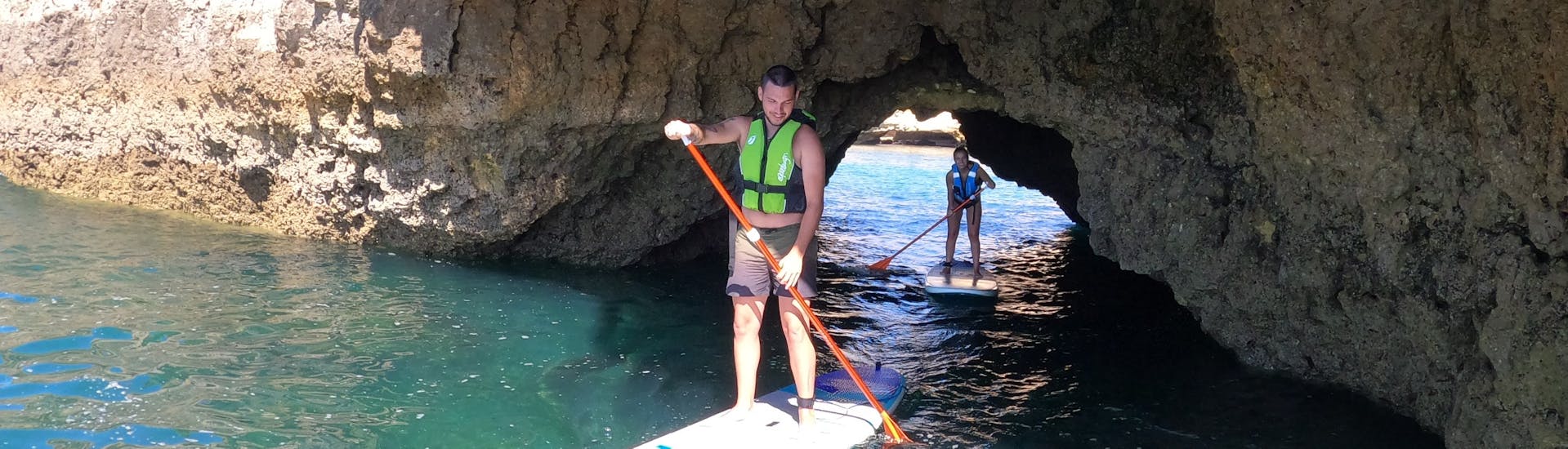 A young man is doing stand up paddle during a Guided Stand Up Paddle Tour along the Albufeira Coast with with SUPA Sea Adventures Algarve.