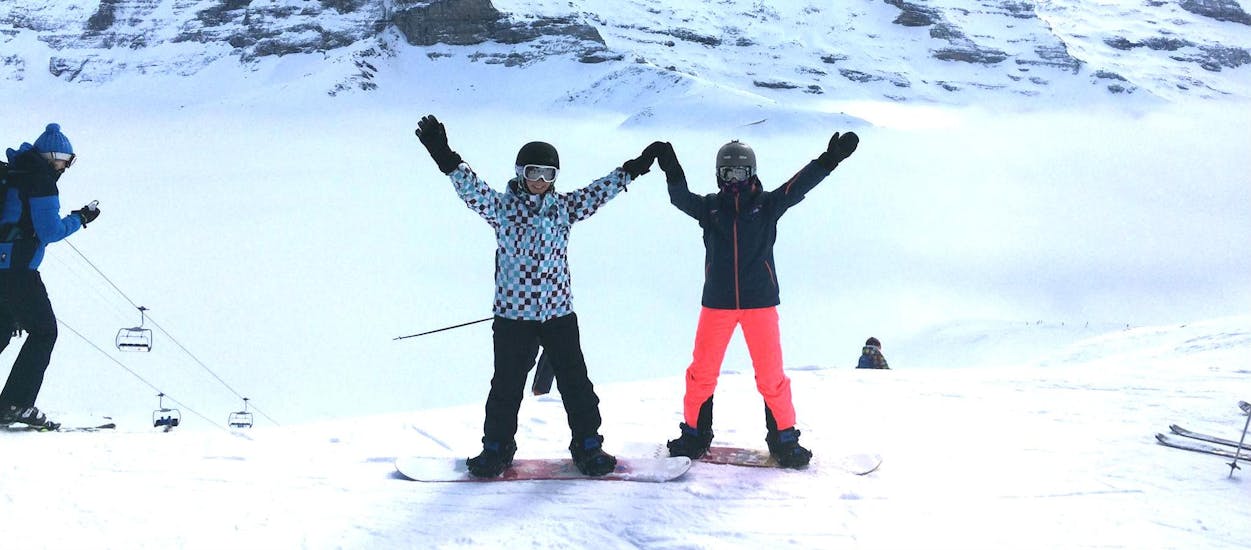 Twee snowboarders juichen bij snowboardles (vanaf 8 jaar) voor beginners.
