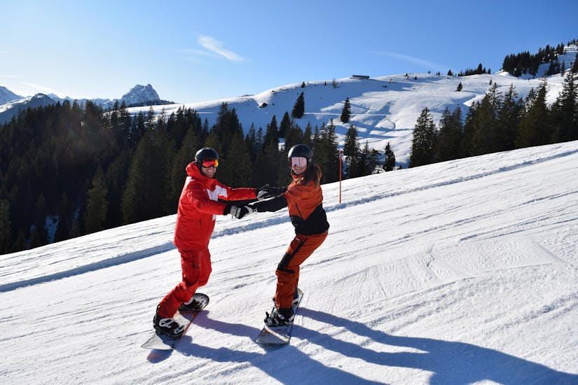 An instructor is helping a snowboarder during private snowboarding lessons for kids and adults of all levels with ski school Snowsports Westendorf.