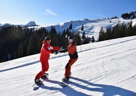 An instructor is helping a snowboarder during private snowboarding lessons for kids and adults of all levels with ski school Snowsports Westendorf.