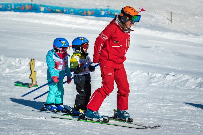 Twee kleine skiërs laten zich tijdens hun kinderskilessen bambini voor beginners voorttrekken door hun skileraar van de skischool Grindelwald in het Kinderland.