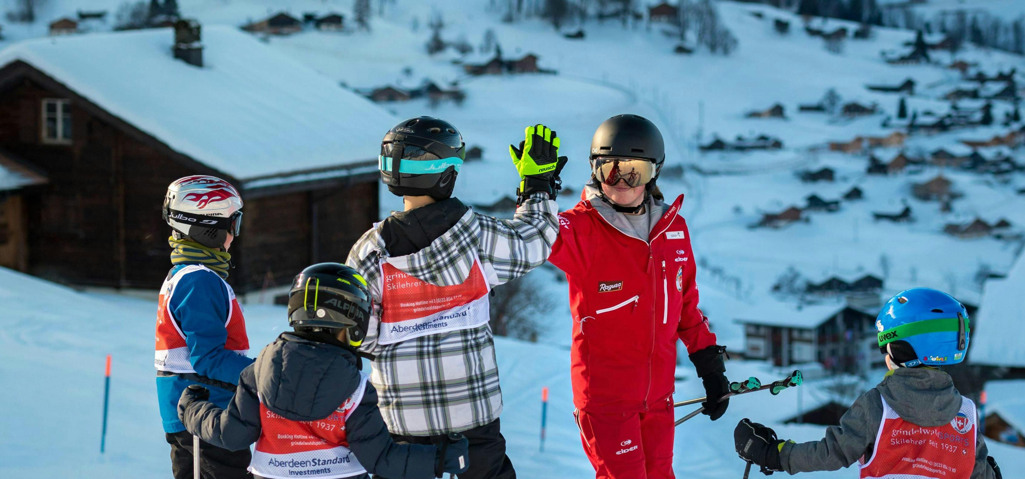 Kids Ski Lessons (6-15 y.) for First Timers from Swiss Ski School Grindelwald A group of skiers give their instructor a high-five during their kids ski lessons for beginners with the Grindelwald Ski School.