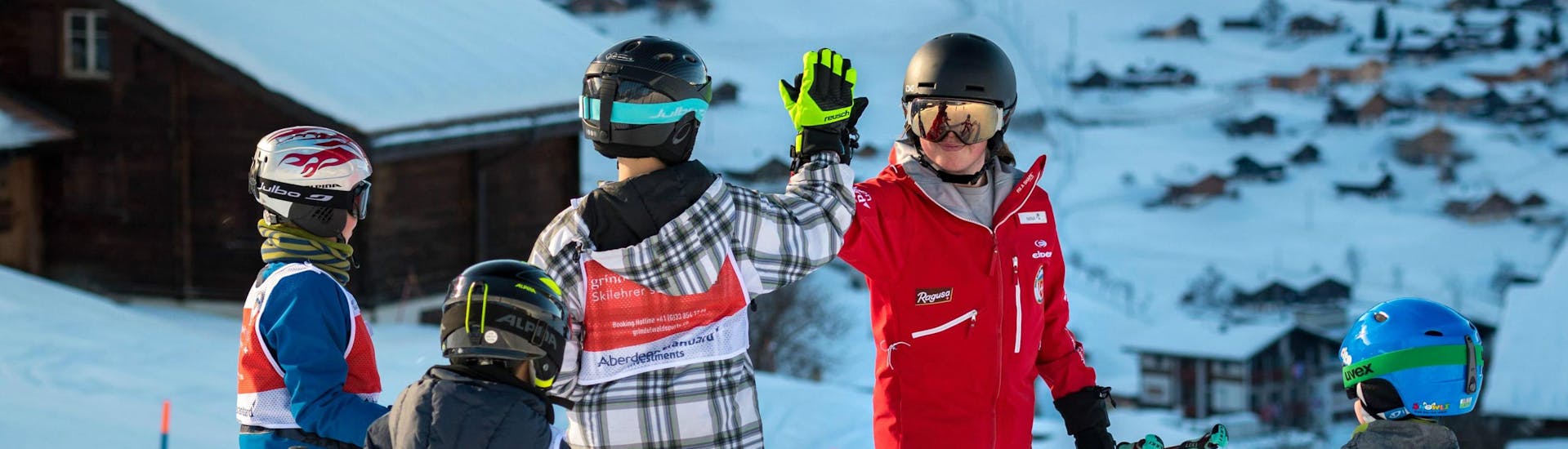 Un gruppo di giovani sciatori si diverte durante le lezioni di sci per bambini di livello intermedio della Swiss Ski School di Grindelwald e dà il cinque al proprio istruttore.