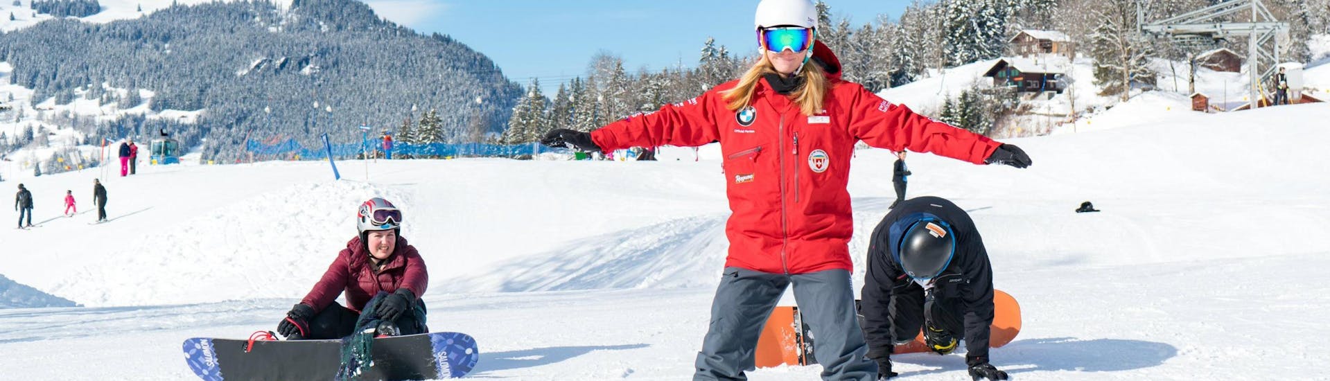 Eine Snowboardlehrerin der Schweizer Skischule Grindelwald macht ihren Schülern während dem Snowboardkurs für Kinder rund Erwachsene für fortgeschrittene Snowboarder Übungen vor.