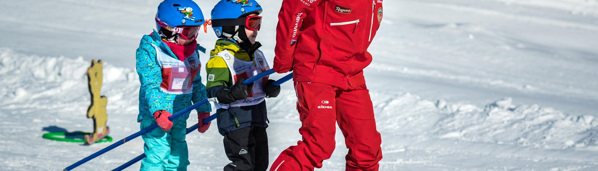Een skileraar van de Zwitserse skischool Grindelwald trekt twee kleine kinderen achter zich aan tijdens een privé kinderskiles voor alle niveaus.