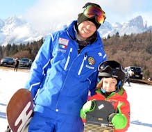 Enfant et moniteur de snowboard à Andalo pendant un cours particulier de snowboard pour enfants et adultes de tous niveaux.