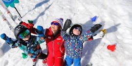Kinderen staan ​​in de sneeuw met hun armen in de lucht naast hun skileraar van de skischool ESF Alpe d'Huez tijdens hun Kids Ski Lessen "Kinderchalet" (2-5 jaar).