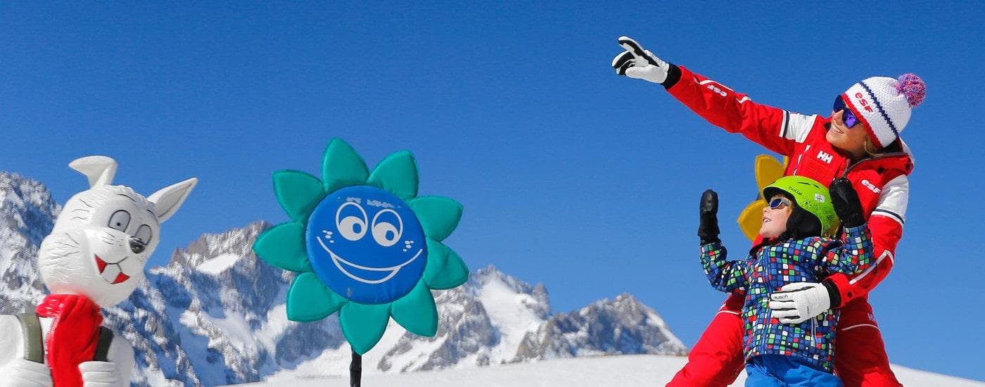 Ein junger Skifahrer und sein Skilehrer von der Skischule ESF Alpe d'Huez spielen zusammen während des Kinderskikurses "Club Piou-Piou" (3-5 Jahre).