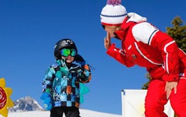 Ein Kind gibt seinem Skilehrer von der Skischule ESF Alpe d'Huez ein High Five während des Kinderskikurses "Club Piou-Piou" (3-5 Jahre)
