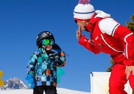 A kid is giving a high five to his ski instructor from the ski school ESF Alpe d'Huez during his Kids Ski Lessons "Club Piou-Piou" (3-5 years).