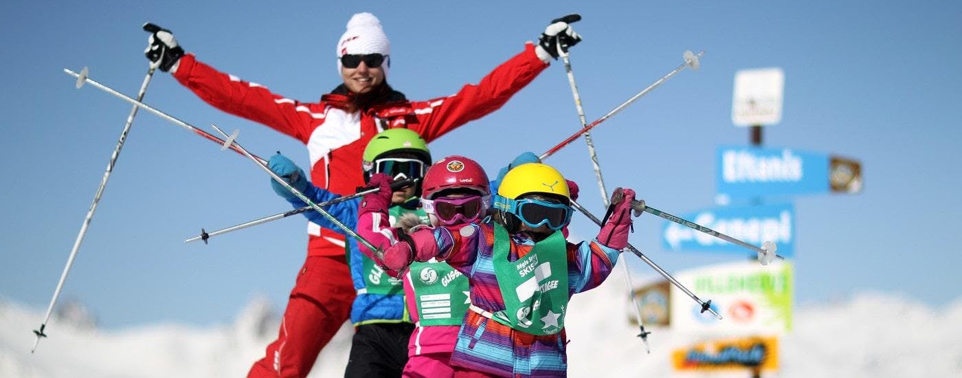 Des enfants se tiennent les uns derrière les autres avec leurs bâtons de ski en l'air pendant leur Cours de ski pour Enfants (6-12 ans) - Débutant avec l'école de ski ESF Alpe d'Huez.
