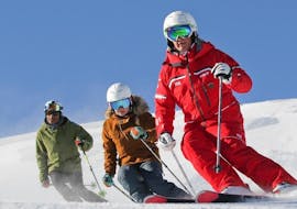 Skiers are skiing down a snowy slope behind their ski instructor from the ski school ESF Alpe d'Huez during their Ski Lessons for Adults - All Levels.