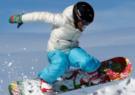 Un snowboarder está dando un salto durante sus clases de snowboard para niños (8-12 años) - Todos los niveles, con la escuela de esquí ESF Alpe d'Huez.