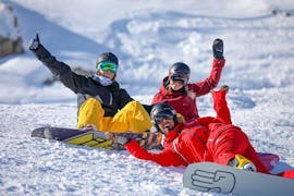Twee snowboarders zitten in de sneeuw rondom hun snowboardleraar van de skischool ESF Alpe d'Huez tijdens hun snowboardlessen voor tieners en volwassenen - alle niveaus.