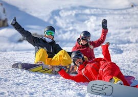 Deux snowboardeurs sont assis dans la neige autour de leur moniteur de snowboard de l'école de ski ESF Alpe d'Huez pendant leur Cours de snowboard pour Ados & Adultes - Tous niveaux.