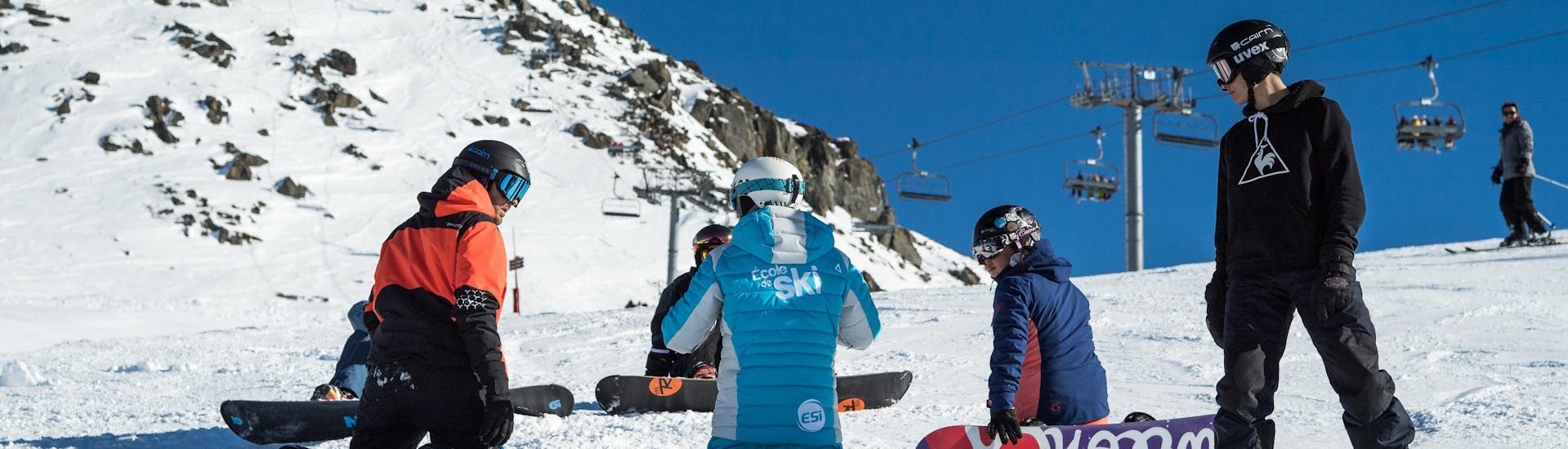 Des snowboardeurs sont assis dans la neige et écoutent les instructions de leur moniteur de snowboard de l'école de ski ESI Gliss'Émotion Super-Besse pendant leur Cours de snowboard pour Enfants & Adultes - Premier cours.