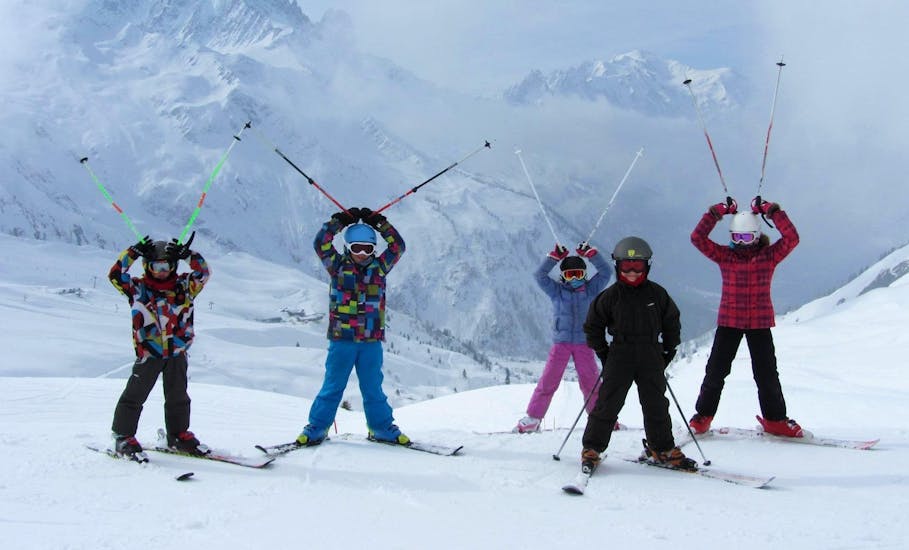 Die Kinder stehen auf dem Gipfel des Berges mit ihren Skistöcken in der Luft, während sie ihren Kinderskikurs (5-12 Jahre) - Anfänger mit der Skischule ESF Chamonix besuchen.
