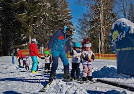 A ski instructor from Skischule Steibis is helping two children on the magic carpet during their Kids Ski Lessons (4-15 years) - Morning - First Timer.