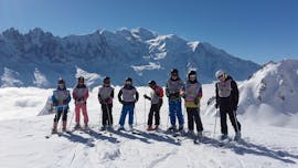 Skiers are standing in line in front of a snow-covered mountain landscape backdrop during their Kids Ski Lessons "Ski Star" (8-12 years) - Holiday with the ski school ESF Chamonix.